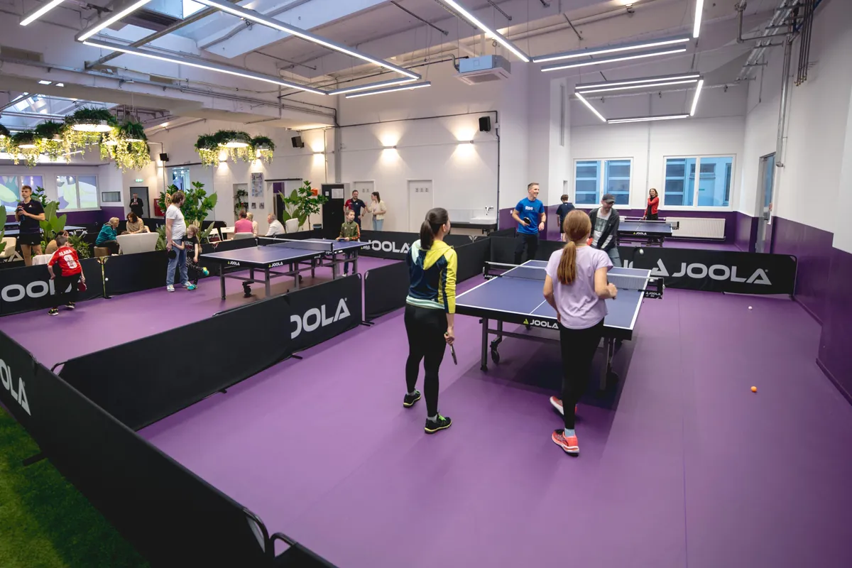 Zwei Schülerinnen spielen Tischtennis in der hellen Halle, im Hintergrund weitere Tische und die Lounge