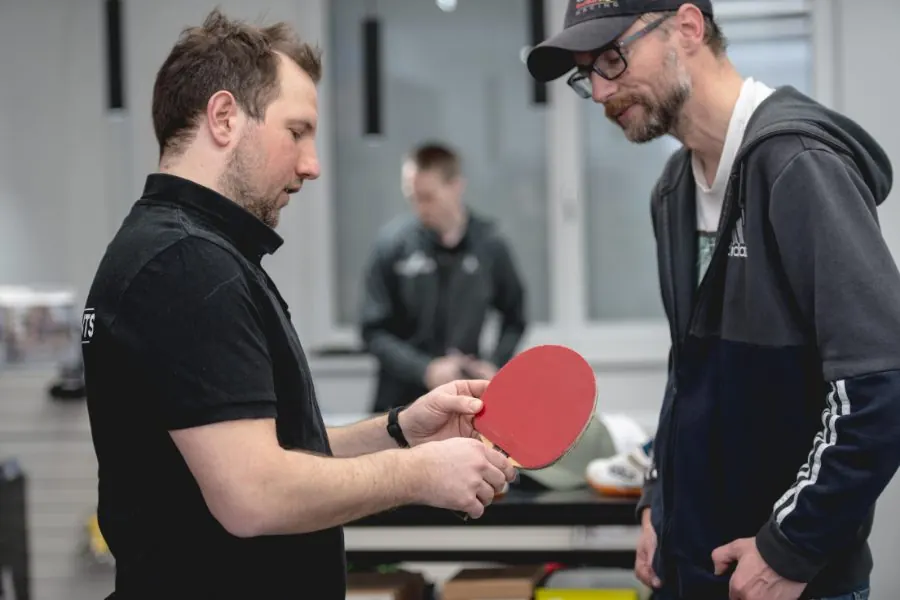 A staff member explains a racket with a red rubber to a customer